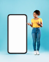Poster - Black woman standing next to huge smartphone, pointing at empty screen, advertising new mobile app, mockup