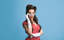 Charming Young Woman In Pinup Outfit Touching Sunglasses, Looking Aside On Blue Background