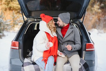 Wall Mural - lovely smiling couple sitting in car trunk in winter forest