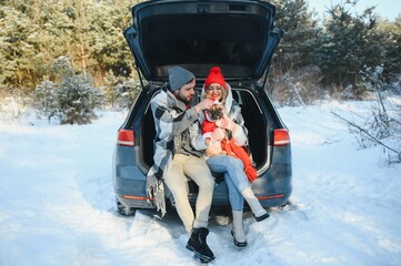 Wall Mural - lovely smiling couple sitting in car trunk in winter forest