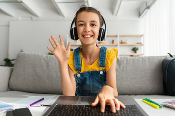 Poster - Girl in headphones using laptop, waving hand to webcam