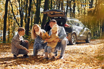 Car is behind. Happy family is in the park at autumn time together