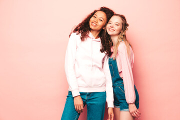 Two young beautiful smiling international hipster female in trendy summer clothes. Sexy carefree women posing near pink wall in studio. Positive models having fun. Concept of friendship