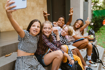 Wall Mural - Multiracial pupils taking selfie photo on mobile phone by school