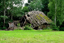 A Close Up On A Damaged, Destroyed, And Dilapidated Barn, House, Or Shack With A Thatch Roof Covered With Moss And Grass Seen In The Middle Of A Public Park On A Polish Countryside In Summer