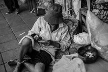 Homeless Beggar Writes Something In His Notebook., Black And White Photo.
