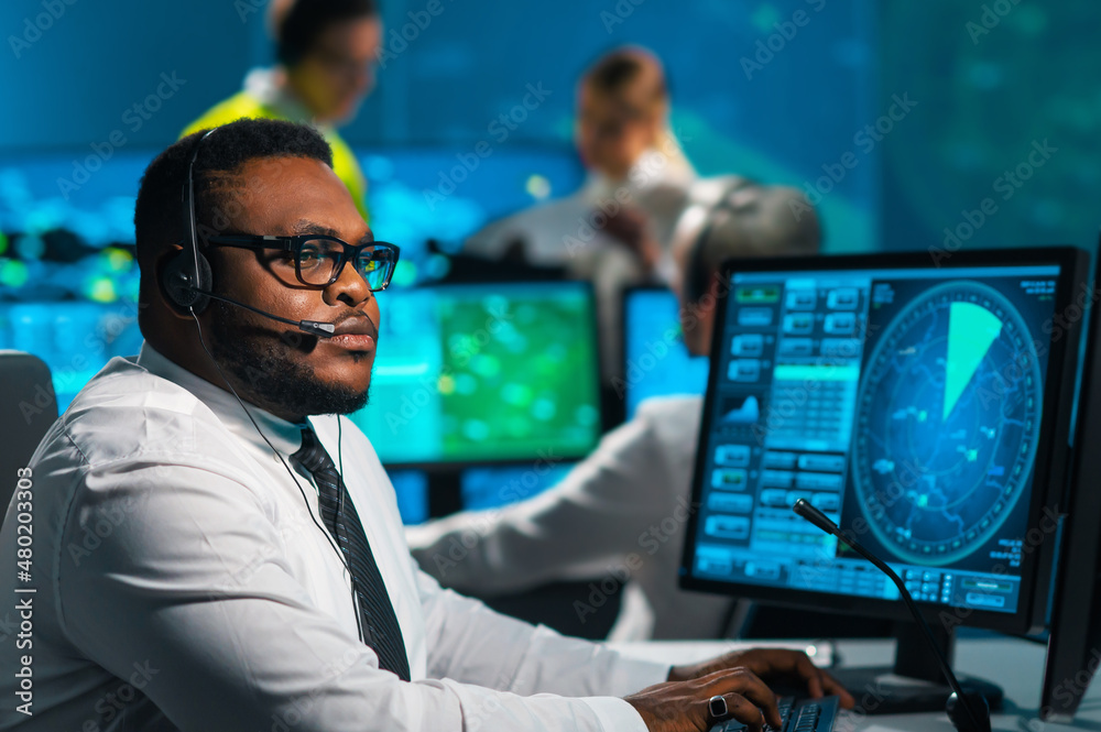 Aircraft flight control officer monitors the approach of aircraft from control tower. Air services office is equipped with navigation systems, radars and computer stations. Aviation concept.