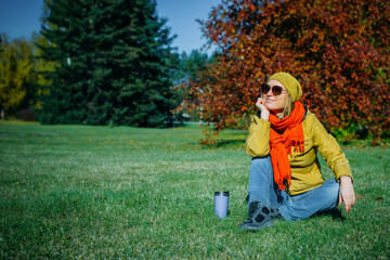 Wall Mural - Attractive woman sitting on green lawn in beautiful park on sunny autumn day. Quiet outdoor recreation, weekend.