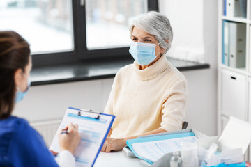 medicine, health and vaccination concept - doctor with clipboard and senior woman in mask at hospital