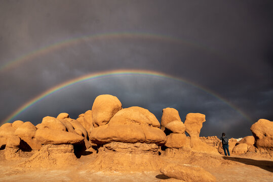 A man takes a photo of a double rainbow over goblin formations in Utah.