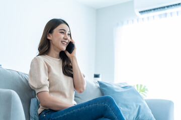 Wall Mural - Asian beautiful woman sit on sofa and talk on mobile phone in house. 