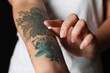 Leinwandbild Motiv Woman applying cream on her arm with tattoos against black background, closeup