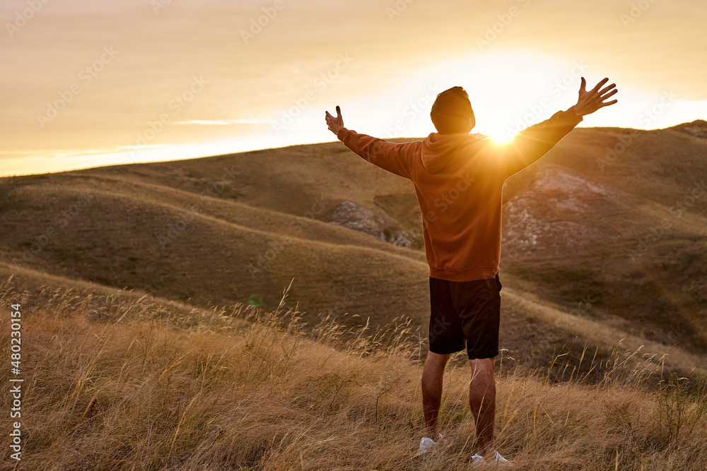 rear view on guy on top of mountain reaches for the sun during ...