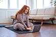 © Roman - Young cute redhead woman preparing for an online fitness class, caucasian fat overweight female in sportstwear sit on mat using laptop. Distance training during the quarantine period