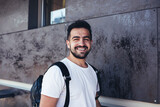 Fototapeta  - Half length portrait of cheerful male tourist dressed in casual white shirt smiling at camera during free time in travel city, happy Caucasian hipster guy with backpack posing at urban setting