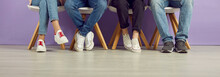 Group Of Young People Waiting In Line. College Students, Classmates And Friends In Jeans And Sneakers Sitting In A Row. Banner Header Background. Cropped Shot, Low Section, Legs And Feet On The Floor