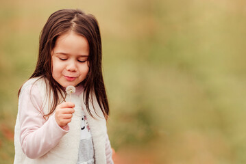 Wall Mural - Little girl blowing a dandelion outdoors in the park