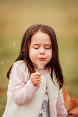 Wall Mural - Little girl blowing a dandelion outdoors in the park