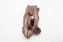 Bottle Of Essential Oil, Tree Bark And Cones On White Background