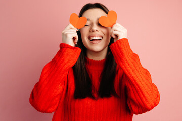 Attractive young woman is covering her face with paper hearts and laughing. The girl is happy and having fun. Concept of the St. Valentine's Day