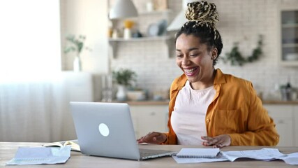 Wall Mural - Overjoyed excited african american girl with dreadlocks, freelancer, manager working remotely at home using laptop, looks at screen with surprise, smiling face, gesturing with hands, got a dream job