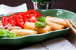 Fried spring rolls, vegetables and tomatoes placed in a green leaf shape plate on a black wooden table and dipping sauce.
