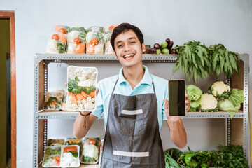 Sticker - Male greengrocer showing vegetables and showing a phone screen