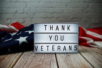 Wall Mural - Thank You Veterans word in lightbox and American flag on wooden background