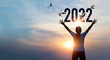 © ipopba - Woman Hands touching of new year 2022 silhouette against with birds of freedom on sunset background, Happy New Year and Hope concept.