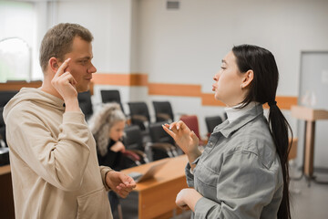 Wall Mural - The girl and the guy talk in sign language. Two deaf students chatting in a university class.