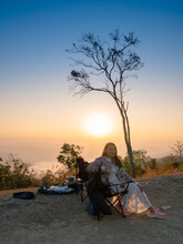 Backlight Soft-focused Of Happy Asian Woman Tourists Sit On Camping Chair Hon Hill With Sunrise View Of Doi Samer Dao Mountain, At Sri Nan National Park Doi Samer Dao. Nan Province, Thailand