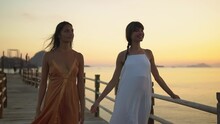 Two Young Woman Models Are Walking In The Evening Pier During Sun Set Time, Evening Dress