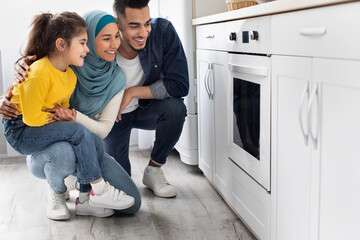 Wall Mural - Middle-eastern family sitting near oven in kitchen and looking inside through glass