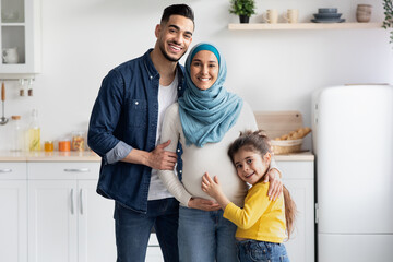 Wall Mural - Islamic Expecting Family. Happy Pregant Muslim Woman Posing With Husband And Daughter