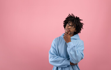 pensive afro teen guy touching his chin, thinking over something on pink studio background, copy spa