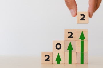 Business concept growth success process in 2022. Close up hand arranging wooden cubes stacking '2022'standing on upwards green arrow in wooden cubes. White background and copy space. Growth banner.