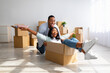 © Prostock-studio - Moving and real estate concept. Joyful african american couple having fun and riding in cardboard boxes at new apartment