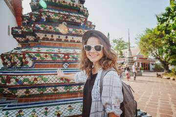 Young happy cheerful woman tourist in sunglasses in a Buddhist temple in Thailand. Travel to Southeast Asia