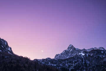 crescent waning moon in purple sky overy mountain peaks