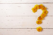 Question mark made from dandelion flowers on rustic white wooden background. Springtime, summertime concept. Copy space.