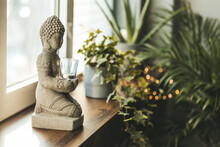 Buddha Statue Close-up In Beautiful Light. Close Up Of A Buddha Figurine. Modern Decor On A Shelf, A Buddha And A Candle Holder And A Plants In A Pot. Spiritual Awakening
