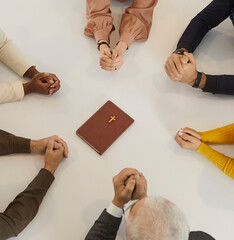 Wall Mural - Diverse group of different religious multiracial multiethnic people praying to God together. Cropped shot of human hands on table around the Holy Bible. Religion, christianity and discipleship concept