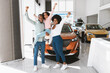 © Prostock-studio - Full length of excited African American family lifting hands up, celebrating new car purchase at auto dealership
