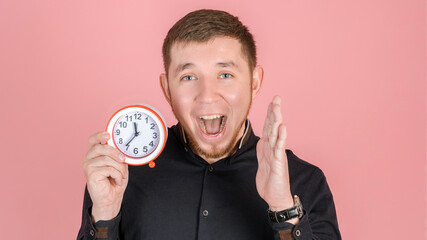 A bearded man screams with his mouth wide open holding an alarm clock near his face, close-up