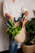 © Dina - woman in white shirt and jeans holding an eco jute reusable bag with bunch of green basil and lettuce. Grocery shopping for vegetables - healthy lifestyle