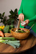 © Dina - Woman in green shirt cooking a salad at home in the kitchen. making vegan dinner or lunch with fresh vegetables. Healthy and eco conscious vegetarian lifestyle.