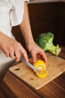 © Dina - Woman slicing a lemon on cutting board and glass of water and veggies on table - healthy lifestyle. Cutting lemon while cooking at home.