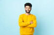 © luismolinero - Young Moroccan man isolated on blue background keeping the arms crossed in frontal position