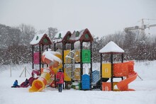 Colorful Playground For Children On Beach On Winter Day. Children Are Playing, Mother Is Standing By Them. It's Snowing Heavily.