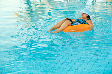 Wall Mural - A woman in a swimsuit and a sun hat in the pool in a swimming circle with a laptop and a cocktail in her hands.